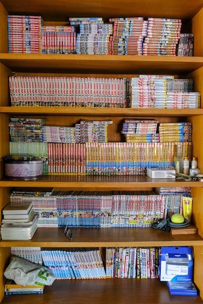 A wide shot of a well-organized manga collection on a bookshelf. The shelves are clean, and the manga volumes are neatly arranged in chronological order by series. The lighting is soft and indirect, highlighting the vibrant covers of the manga.