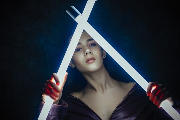A close-up shot of a cosplayer dressed as a fantasy mage, holding a glowing staff. The staff is intricately designed with swirling patterns and embedded crystals. The cosplayer's face is partially obscured by a hood, but their eyes are visible, glowing with a hint of magical energy.