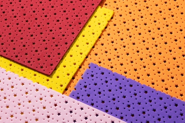 A close-up shot of different types of EVA foam sheets and rolls, showcasing their textures and thicknesses. Tools like a heat gun, craft knife, and cutting mat are visible in the background, suggesting their use in shaping the foam.