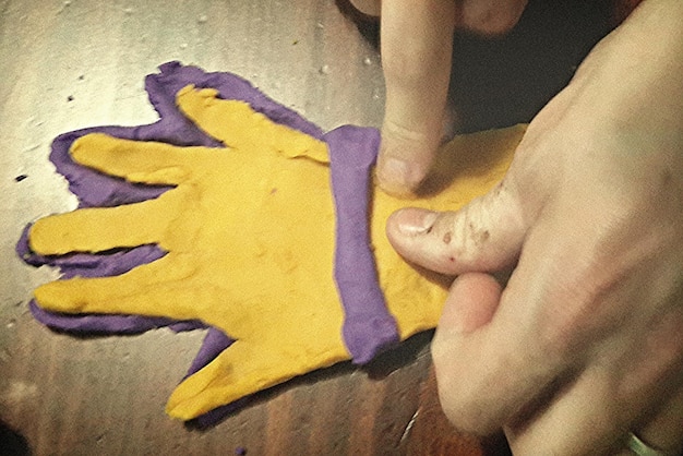 Close-up of a crafter's hands carefully applying super glue to a small, detached piece of EVA foam on a cosplay prop. The focus is on precision and control, with the glue nozzle held close to the foam's surface.