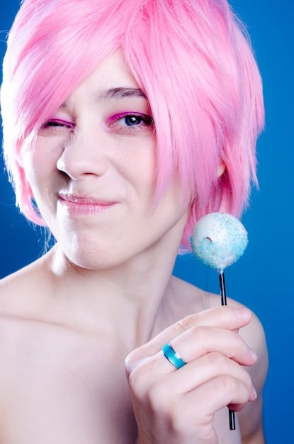 A close-up of a cosplayer's hands meticulously styling the bangs of a bright pink anime wig with a comb and hairspray, showing focus and precision.